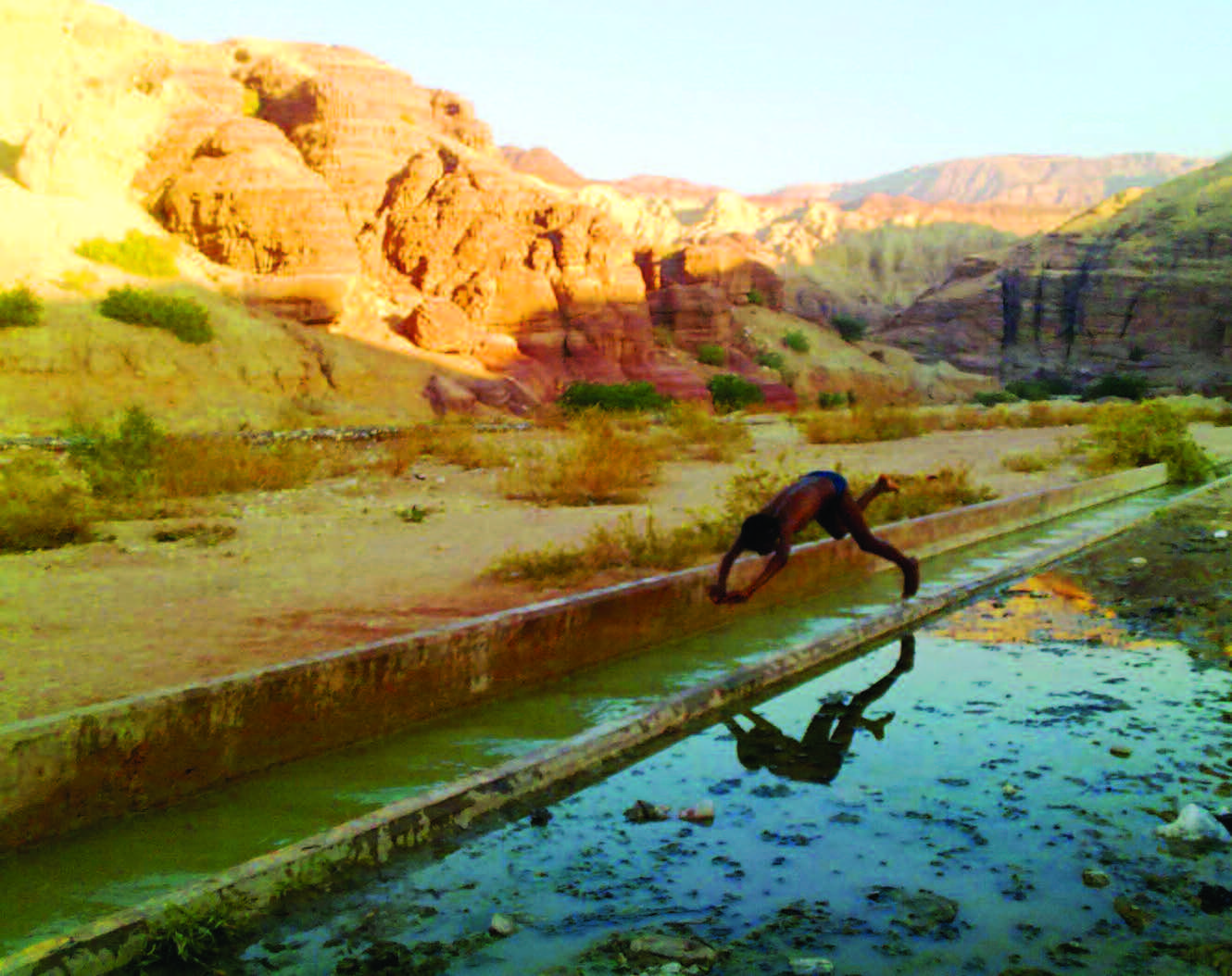 Boy jumping in irrigation canal in arid area